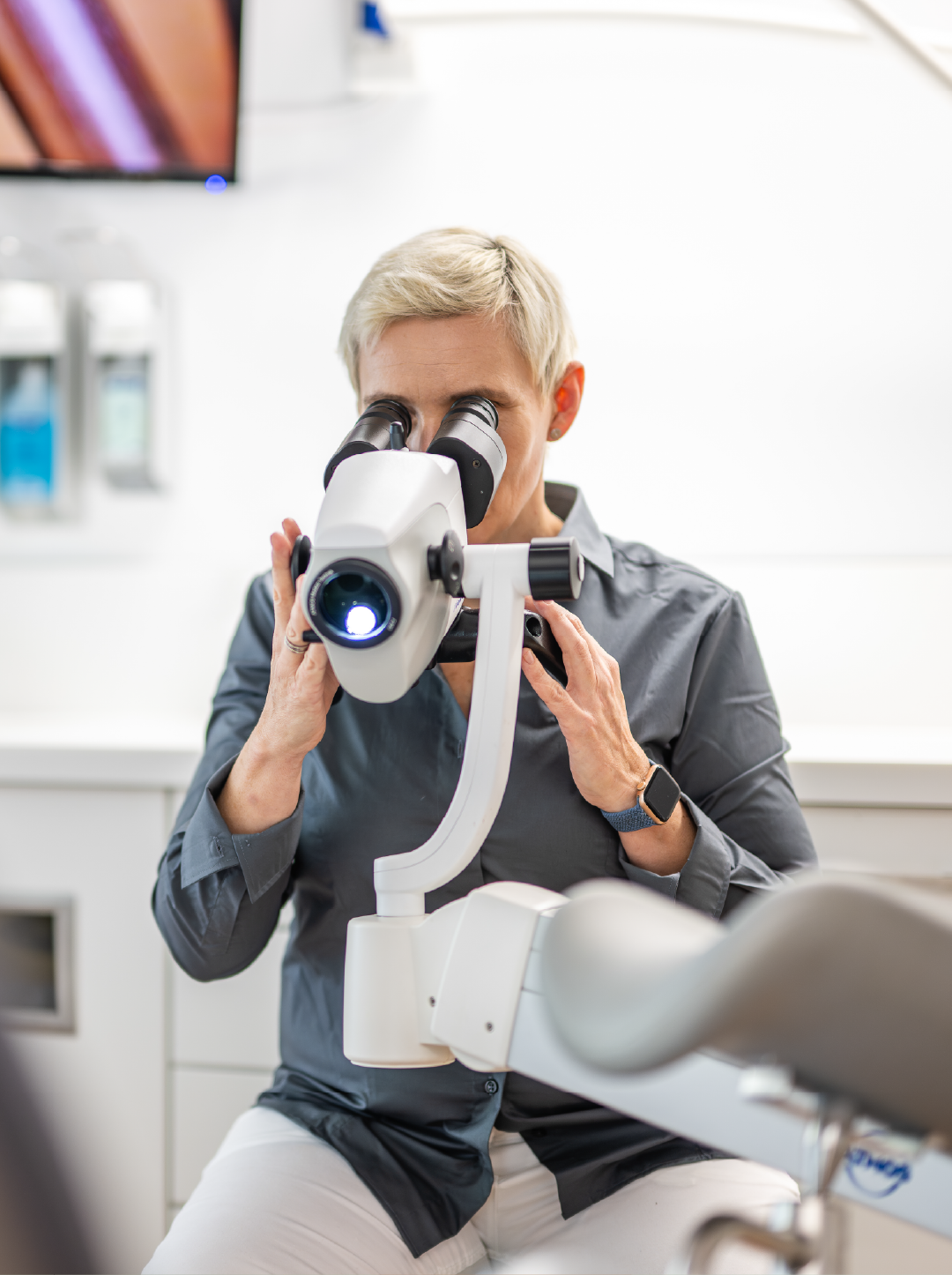 Eine Frau betrachtet durch ein Mikroskop in einer modernen medizinischen Umgebung.
