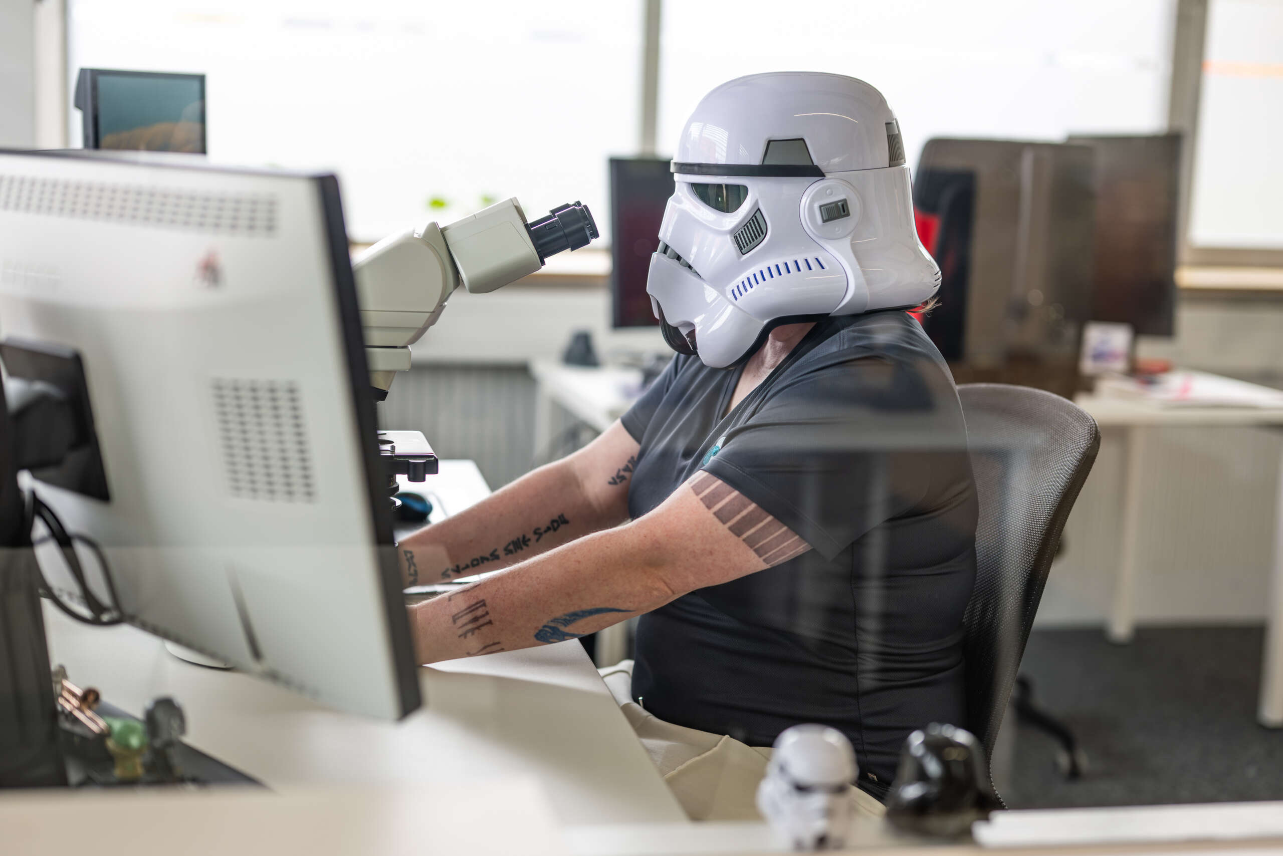Person trägt einen Stormtrooper-Helm und arbeitet am Mikroskop in einem modernen Büro.