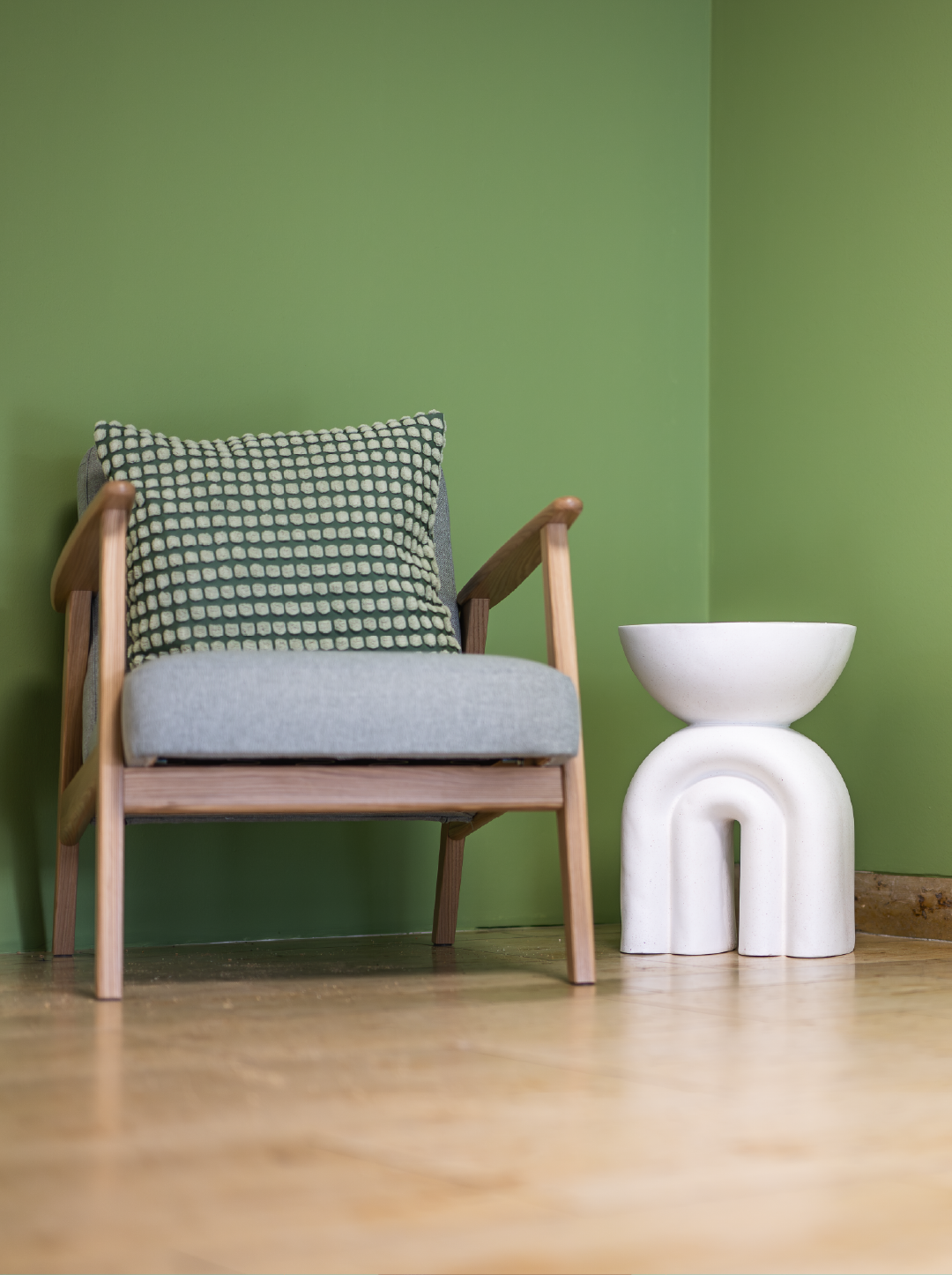 Ein Holzstuhl mit einem gepolsterten Kissen und einem weißen Beistelltisch in einem Raum mit grüner Wand.
