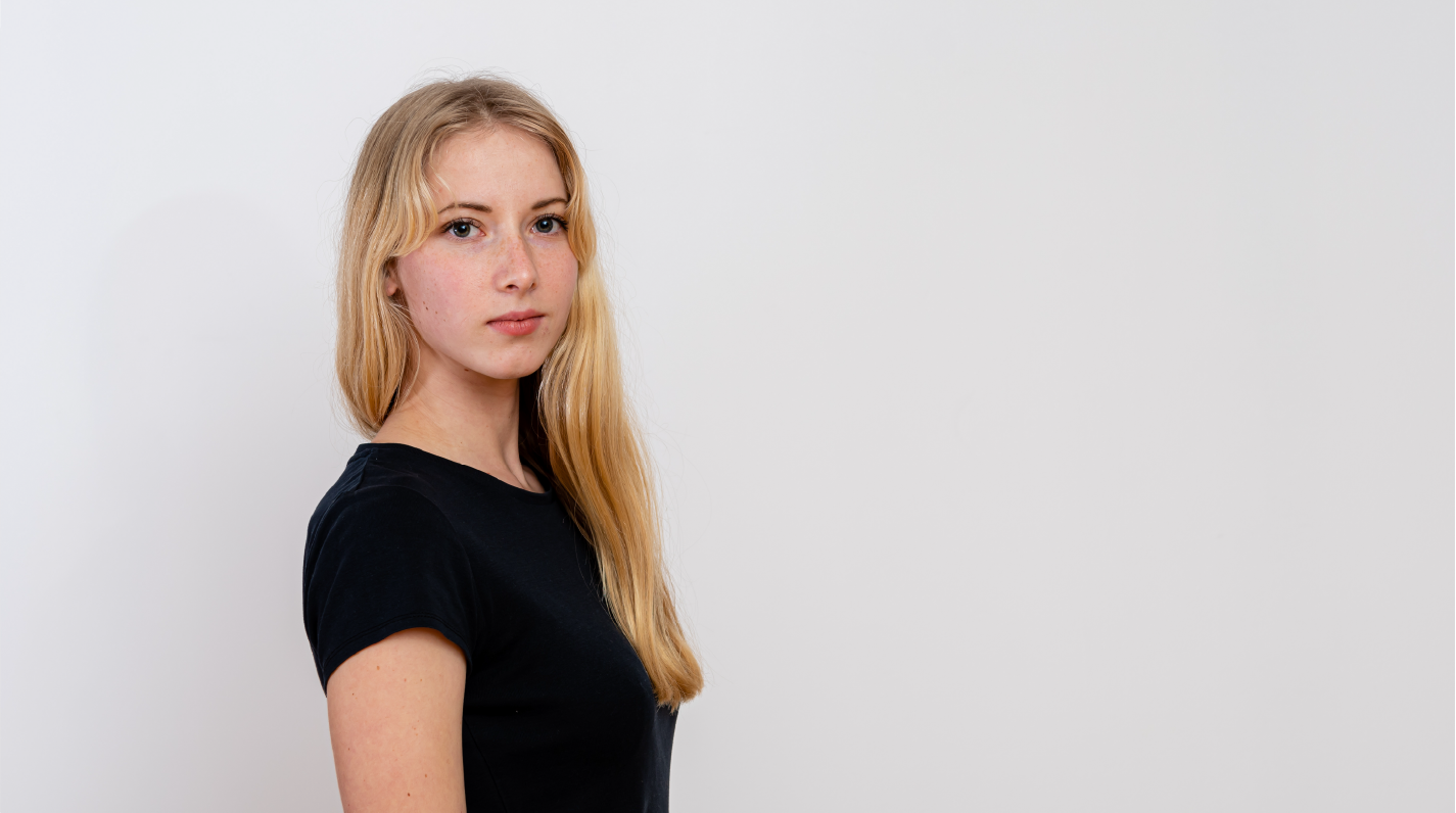 Junge Frau mit langen blonden Haaren, die in einem schwarzen T-Shirt zur Seite schaut.