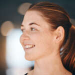 Frau mit roten Haaren und Sommersprossen, die lächelt und zur Seite schaut.